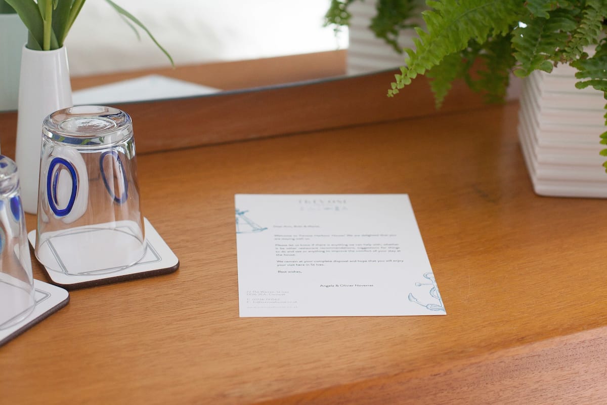 A neatly arranged hotel room with a bed, a wooden nightstand, a vase with white flowers, a glass of water, and a fern plant.