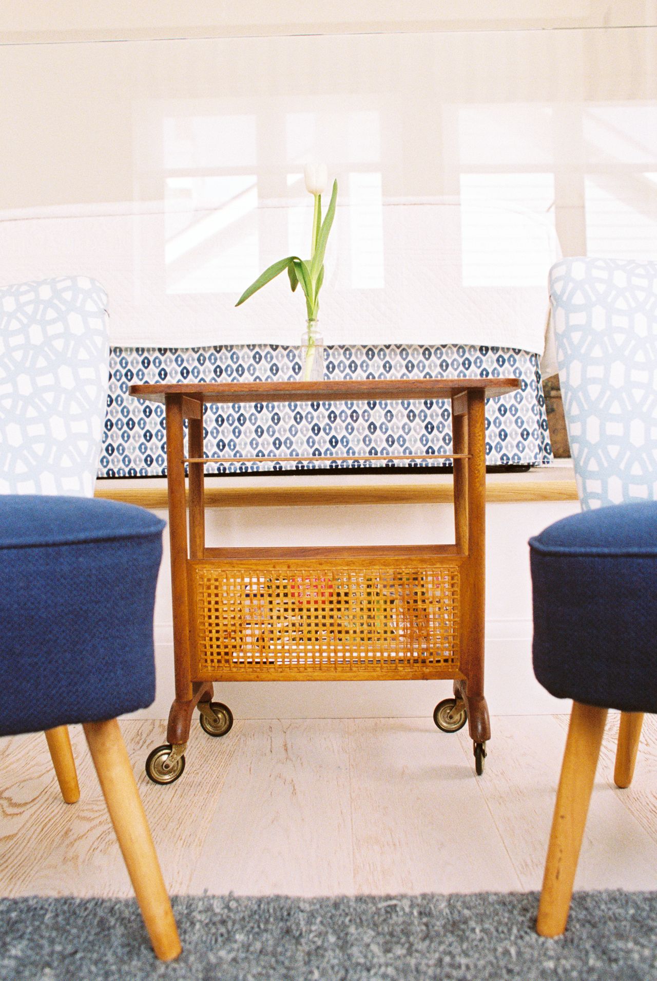 A small wooden cart with a woven basket, two blue upholstered chairs, and a patterned tablecloth.