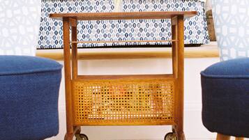 A small wooden cart with a woven basket, two blue upholstered chairs, and a patterned tablecloth.