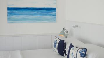 A bedroom with a bed, pillows, a nightstand, a lamp, and a painting of the ocean on the wall.