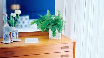 A wooden desk with a potted fern, a glass bottle, and a vase with white flowers.