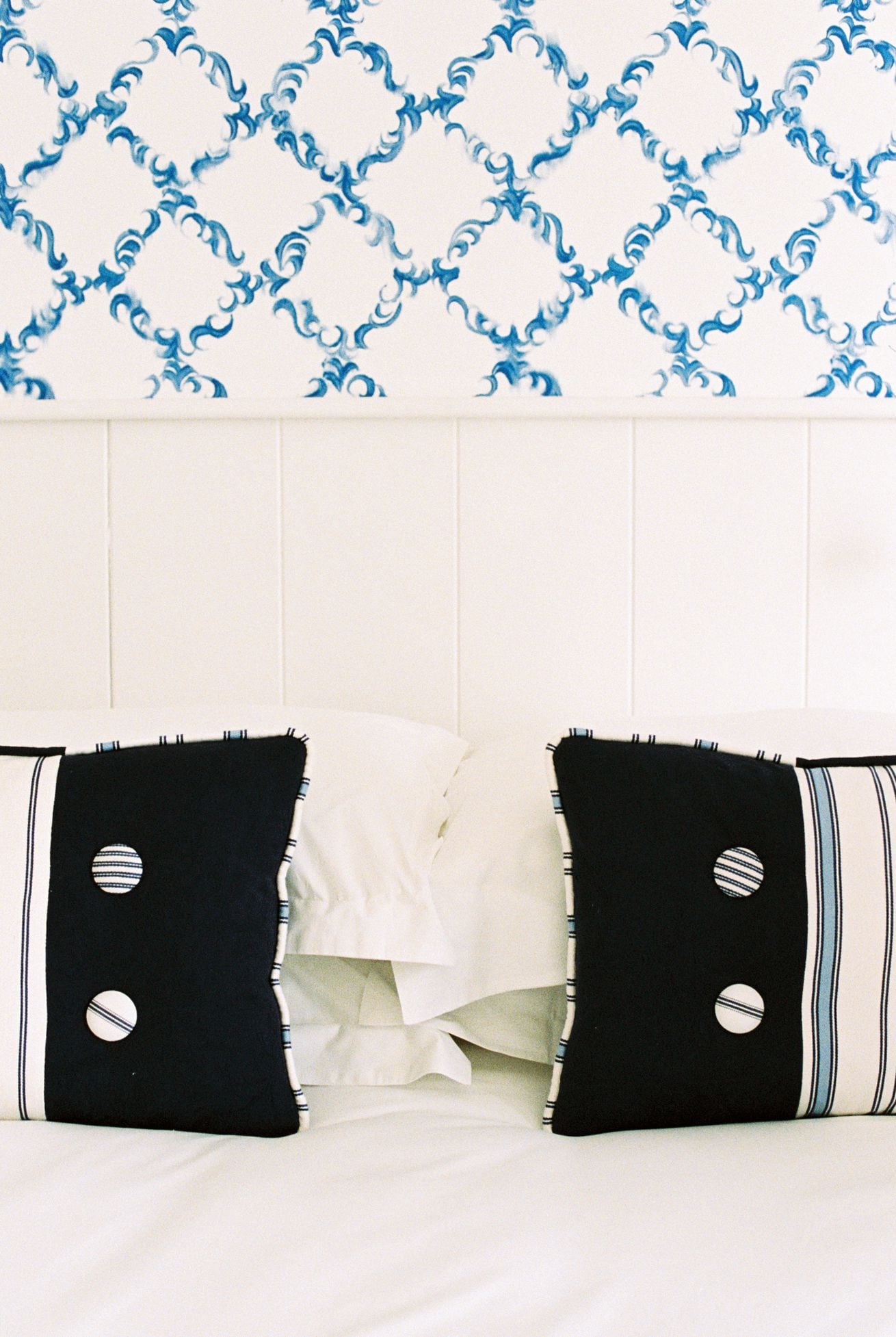 A bed with white bedding and two black pillows with circular patterns.