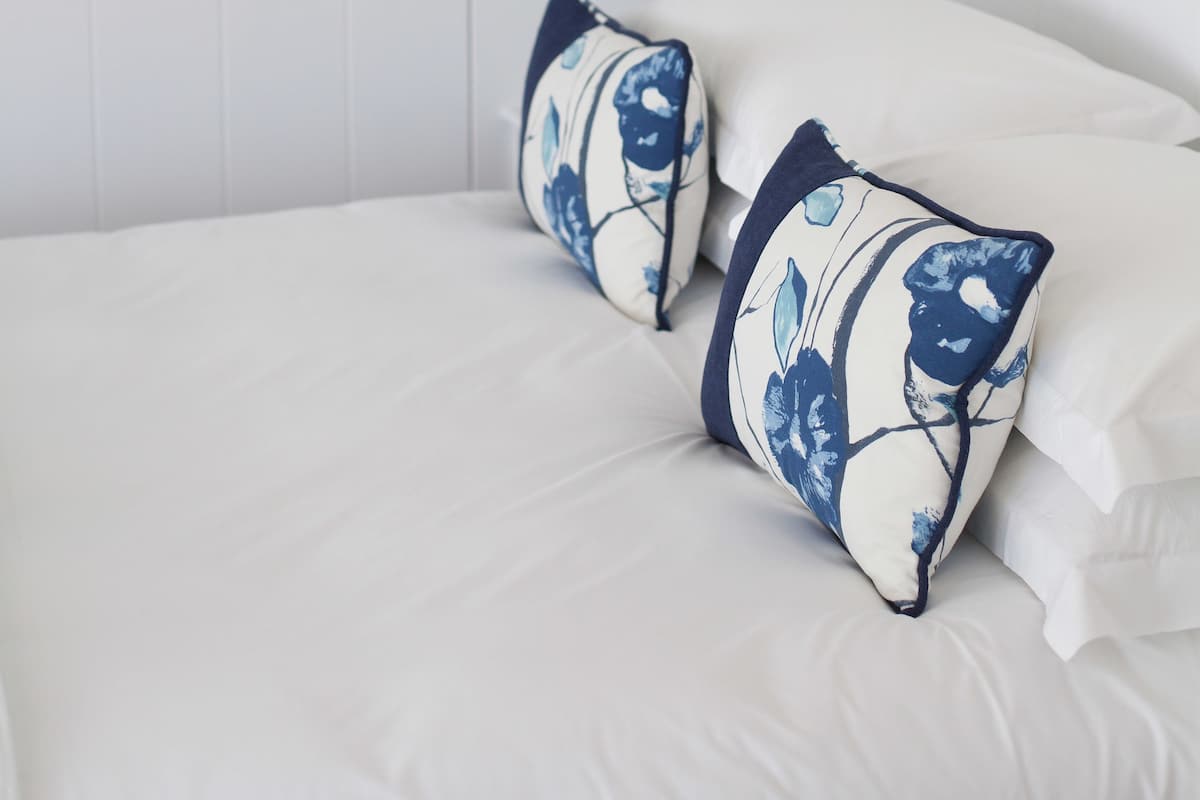 A neatly made bed with white bedding and two decorative pillows with a blue and white pattern.