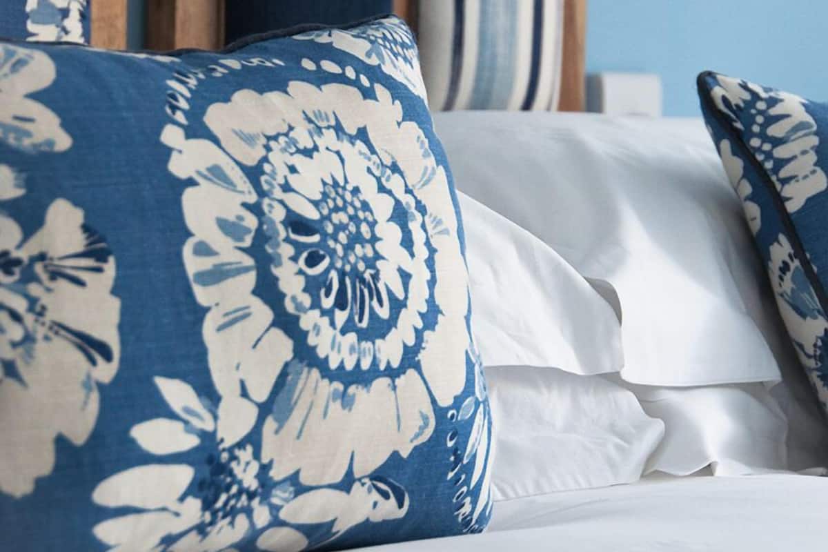 A bed with white linens and blue floral pillows.