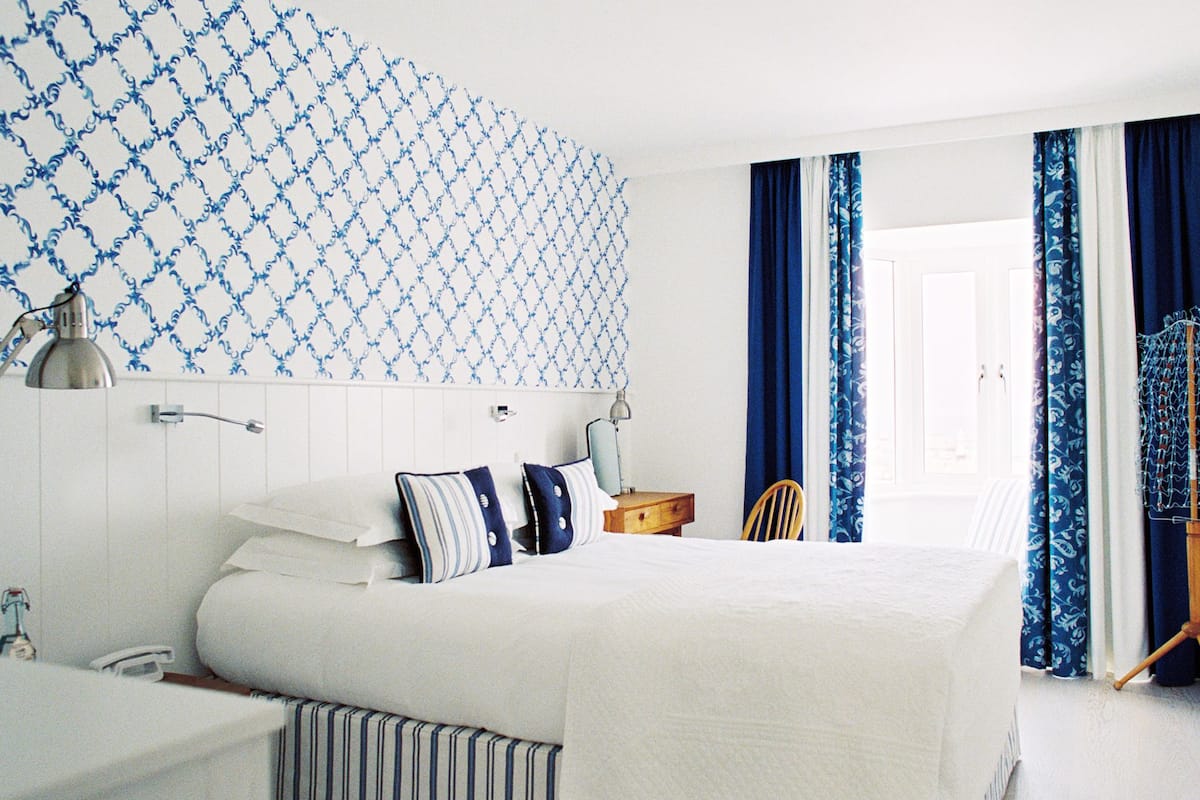 A neatly arranged hotel room with a large bed, bedside lamps, a small wooden nightstand, and a chair.