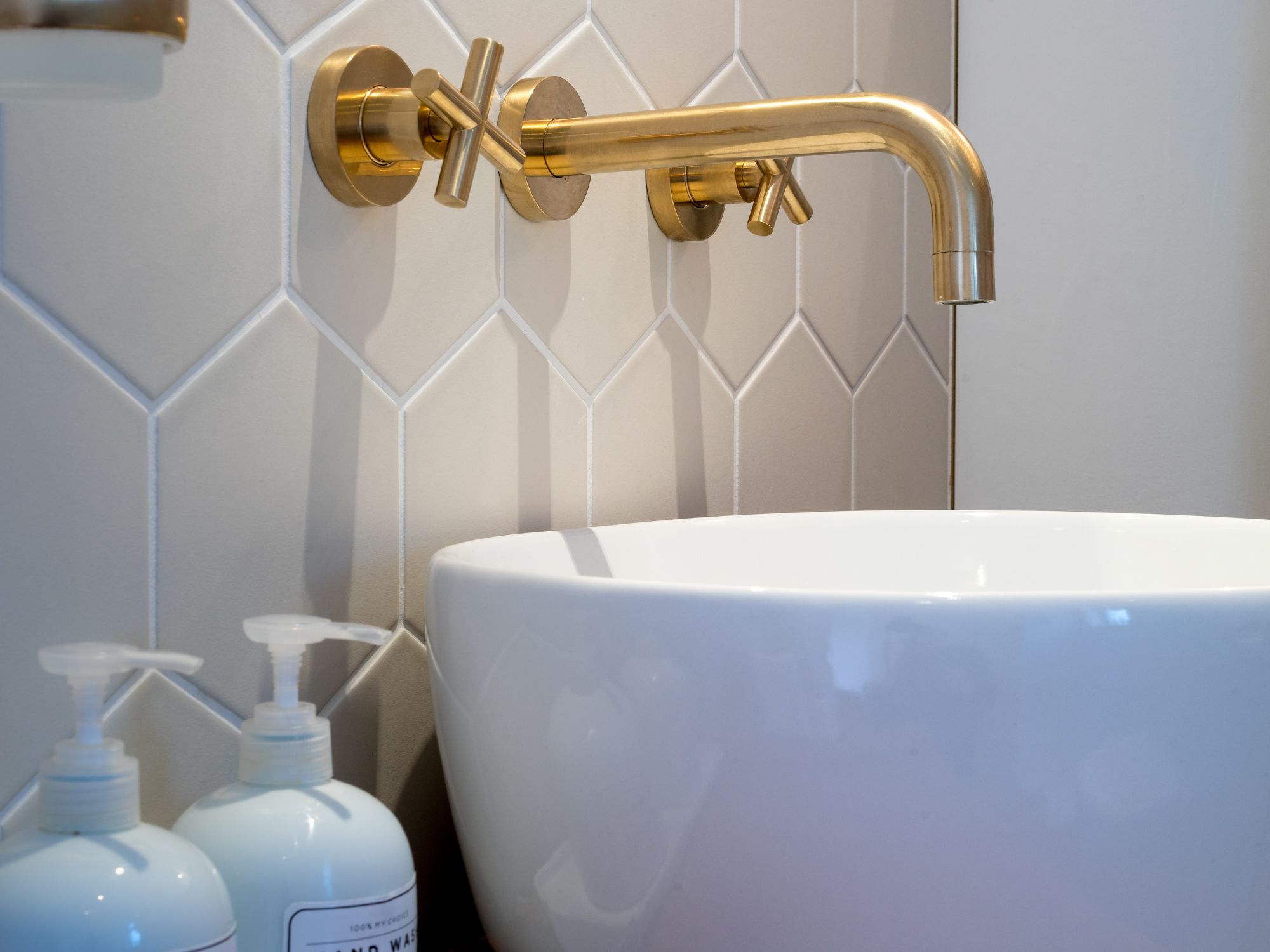 A bathroom with a white sink, gold faucets, and white tiles.