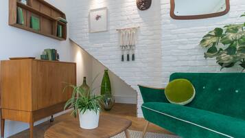 A modern living room with a green sofa, wooden sideboard, and a white brick wall.