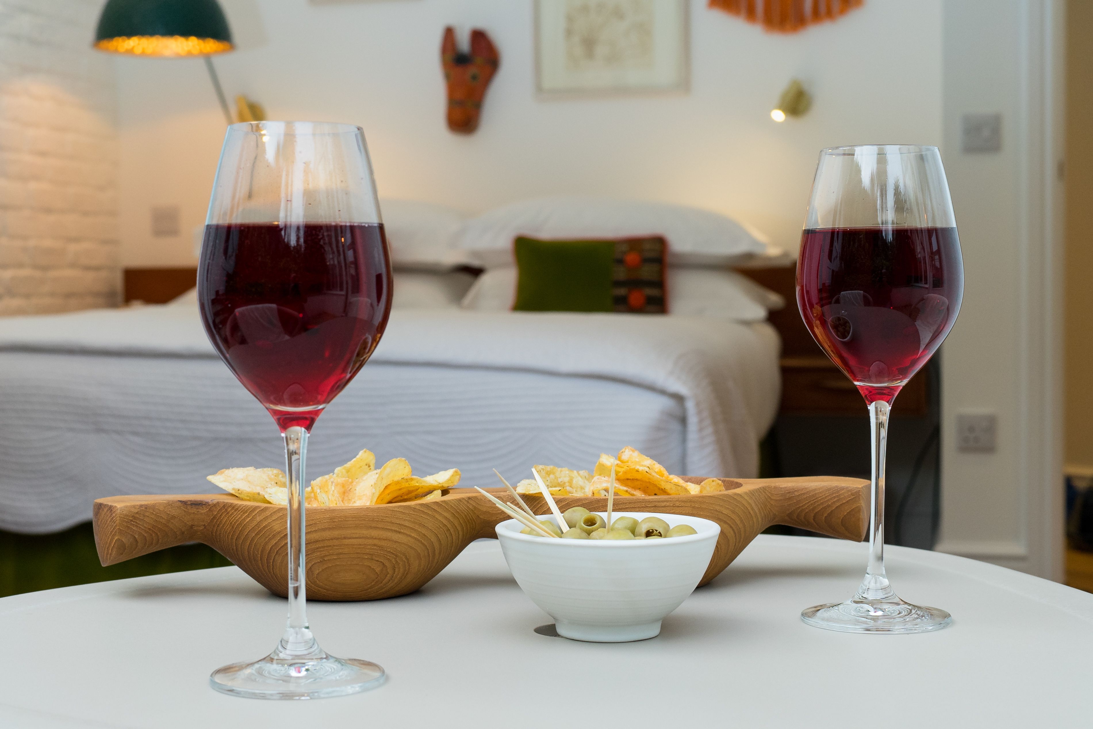 Two wine glasses on a table with a bowl of olives and chips.
