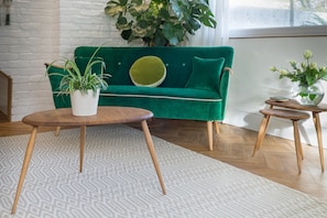 Een groene bank met een rond kussen, een witte plant in pot en een klein houten tafeltje met een bloevas.