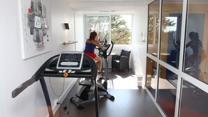 Une salle de sport moderne, équipée de deux vélos d’appartement, ornée d’un grand tableau abstrait et offrant une vue sur l’extérieur grâce à de grandes fenêtres.