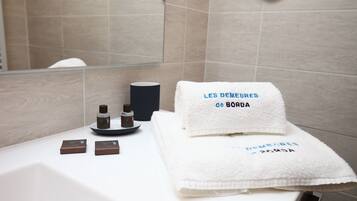 A bathroom with a white bathtub, two brown soap bars, a white towel with text, and a black cup.
