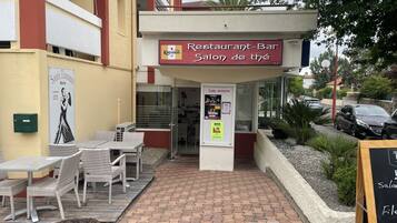 A restaurant with outdoor seating, a signboard, and a small garden area.