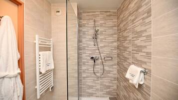 Uma casa de banho moderna com cabine de duche em vidro, uma banheira branca e um porta-toalhas com toalhas.
