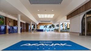 Un hall espacioso con una alfombra azul que muestra el nombre del hotel, un mostrador de recepción y palmeras visibles a través de las ventanas.