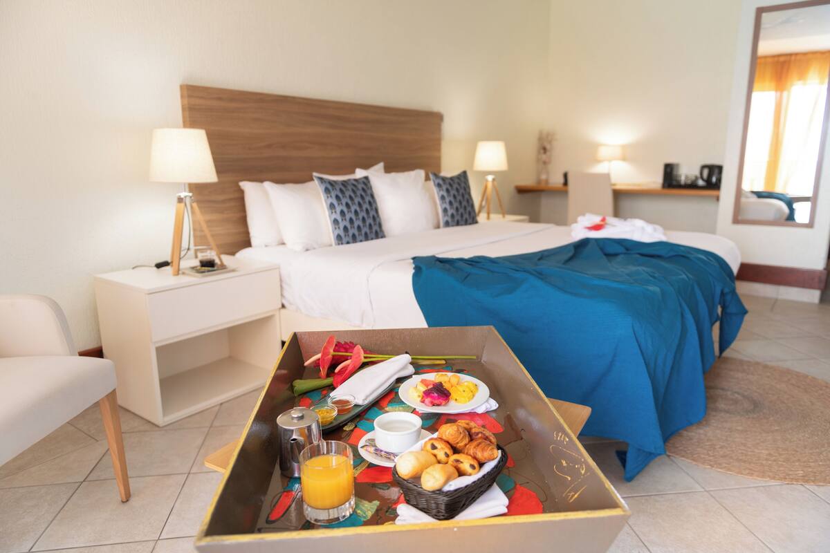 A hotel room with a bed, bedside tables, a breakfast tray with croissants and orange juice, and a nightstand with a lamp.