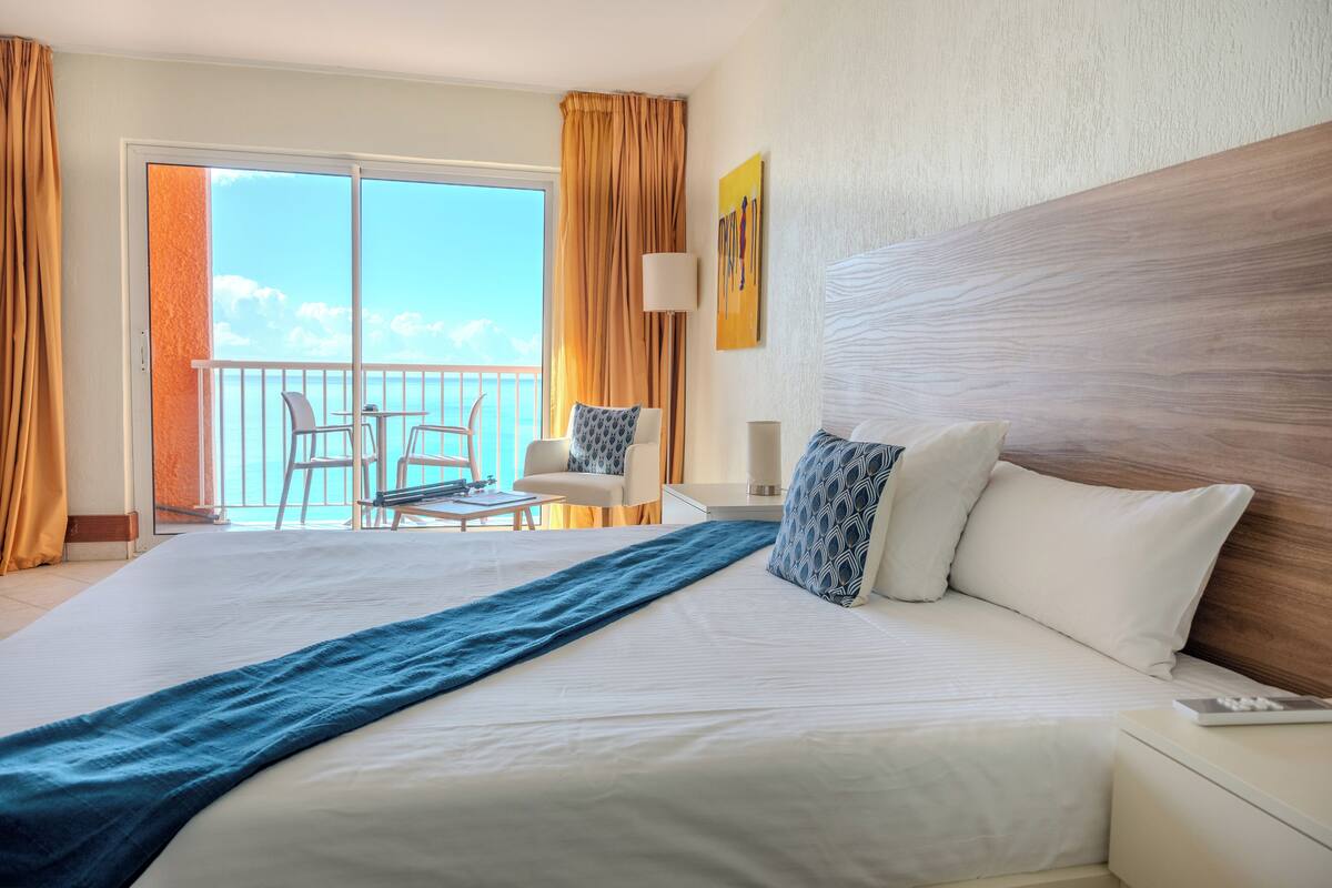 A hotel room with a large bed, a balcony with a view, a desk, and a chair.