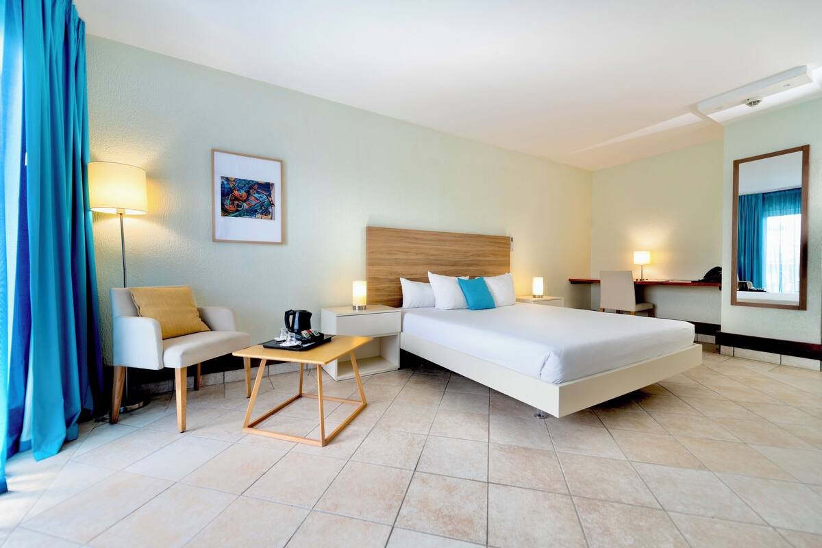 A hotel room with a bed, a desk, a chair, a coffee table, and a lamp.
