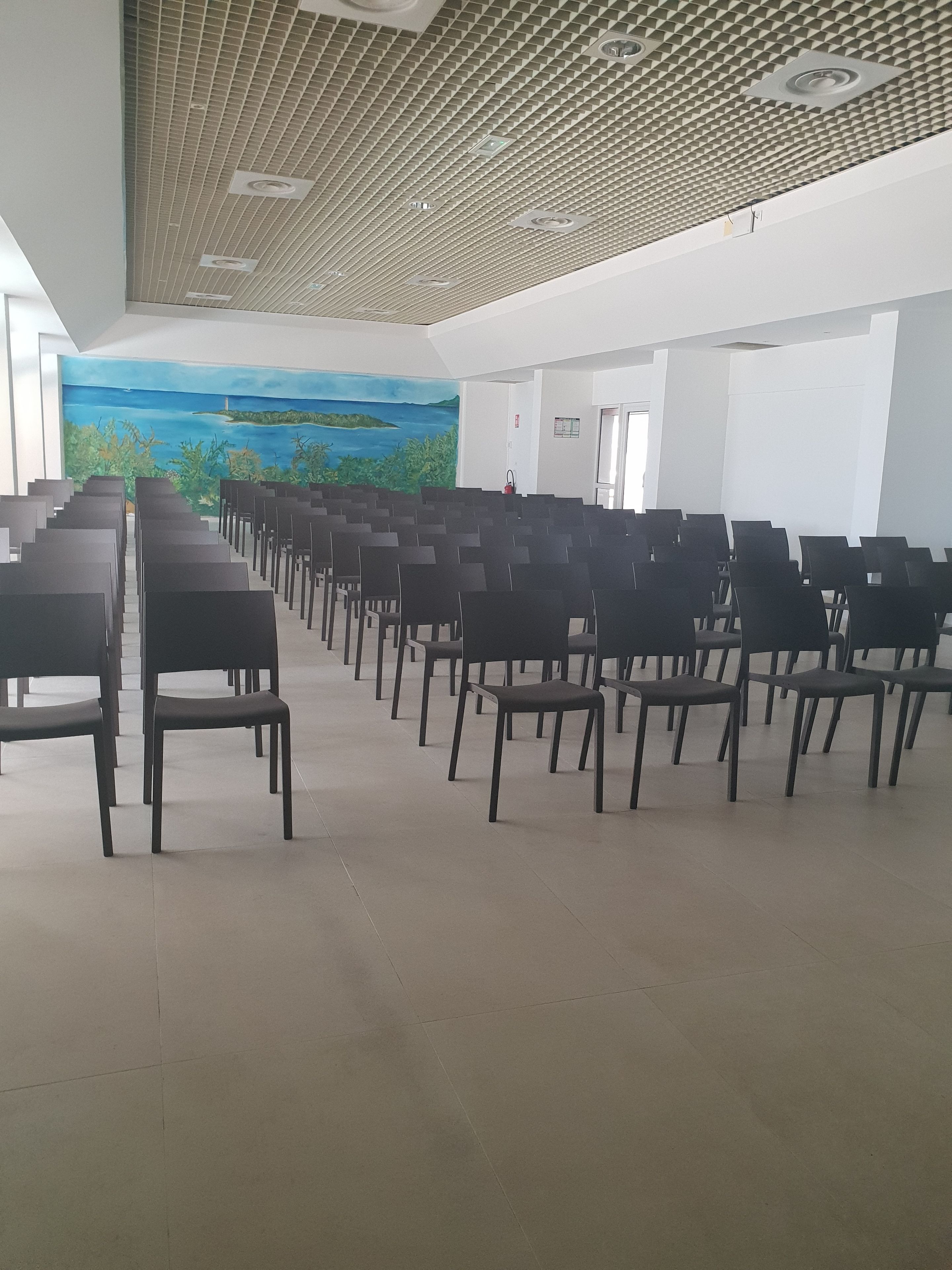 Un salón amplio con filas de sillas negras y un techo con diseño geométrico.