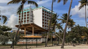 Hotel de varios pisos con un atrio central, rodeado de palmeras y una zona de arena.