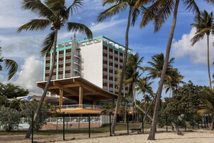 Hotel de varios pisos con un atrio central, rodeado de palmeras y una zona de arena.