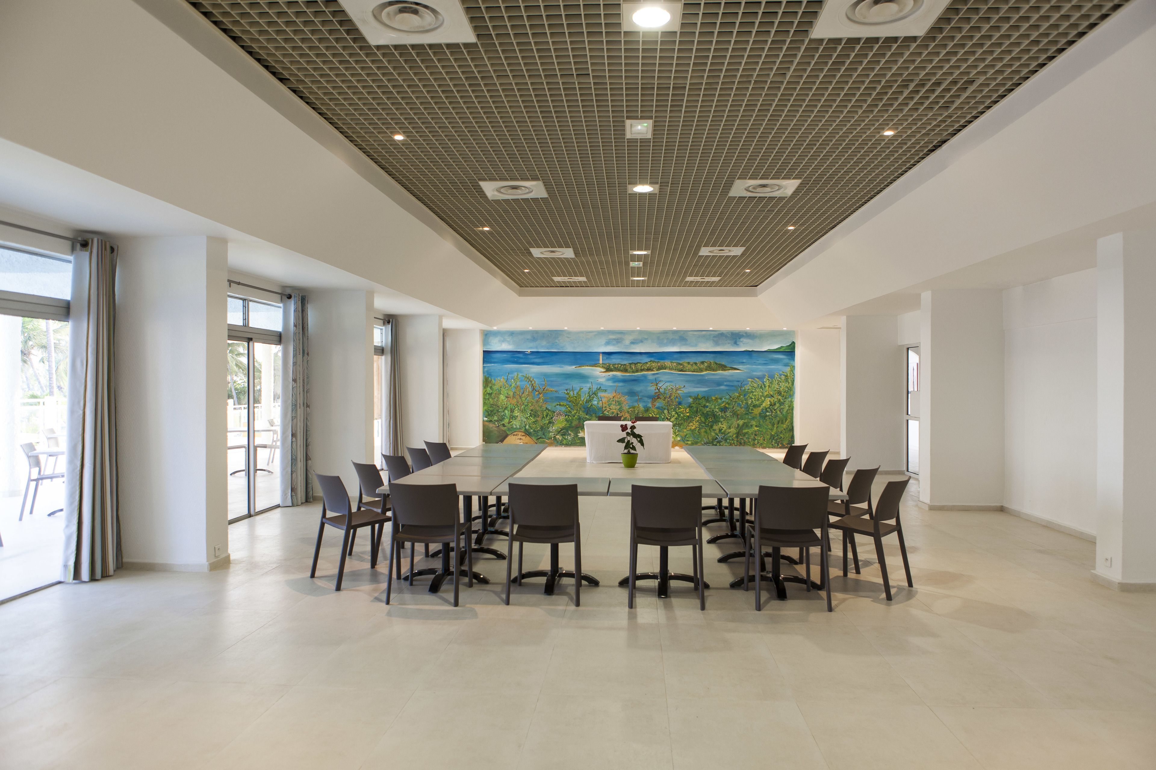 A spacious conference room with a large table and chairs, a ceiling with recessed lighting, and a mural of a landscape on the wall.