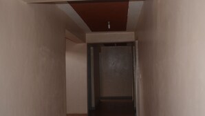 A hallway with a ceiling light fixture, a door at the end, and a tiled floor.