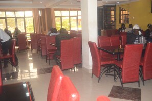 Ein Restaurant mit roten Stühlen und Tischen, großen Fenstern und einem gefliesten Boden.