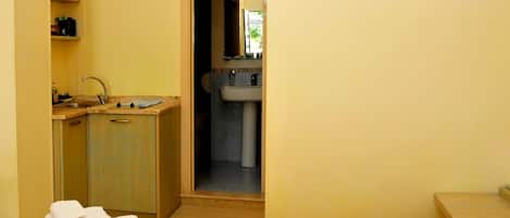 Habitación de hotel con cama, un escritorio pequeño con lavamanos y baño visible a través de una puerta abierta.