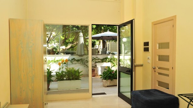 A room with a sliding glass door leading to an outdoor area with plants and a table. There is a bench and a door with a keypad lock. - Camere sul Lungomare (Otranto)