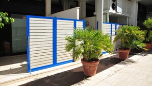 A building entrance with a blue and white gate, potted plants, and a tiled walkway. - Camere sul Lungomare (Otranto)
