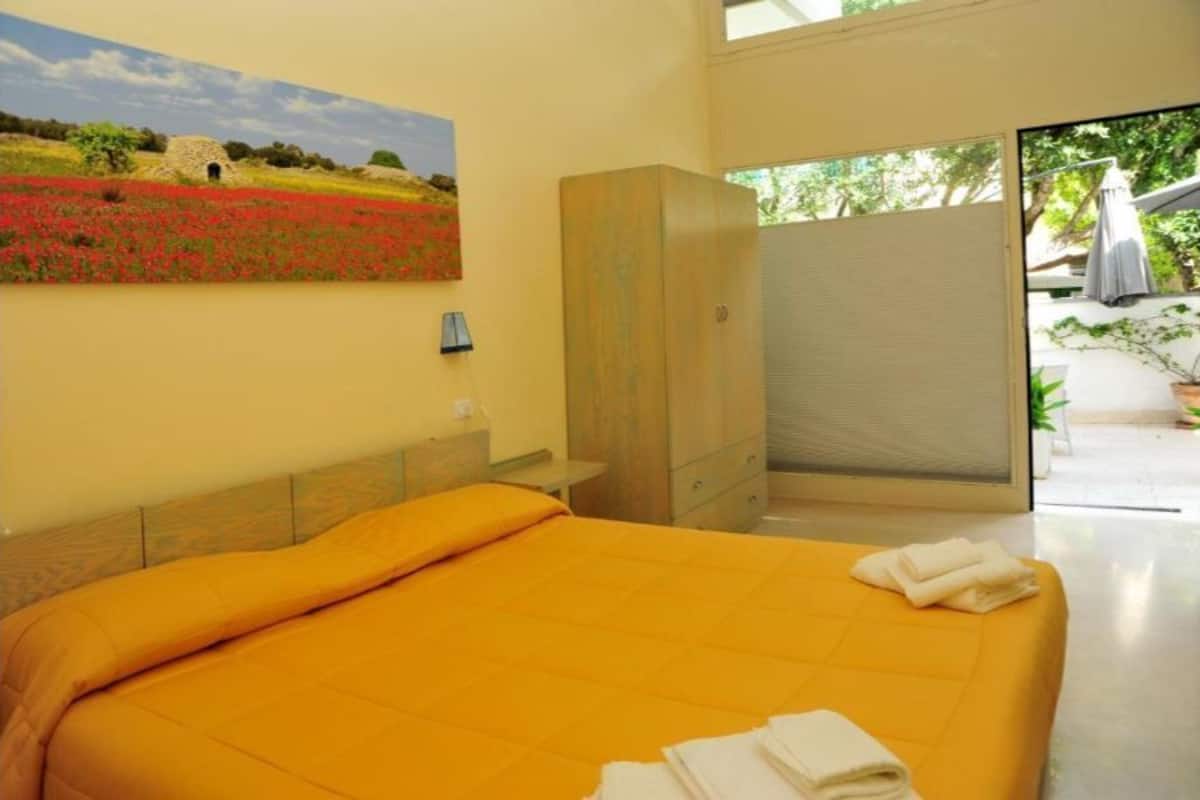 Una habitación con una cama, un cuadro y vista a un jardín.