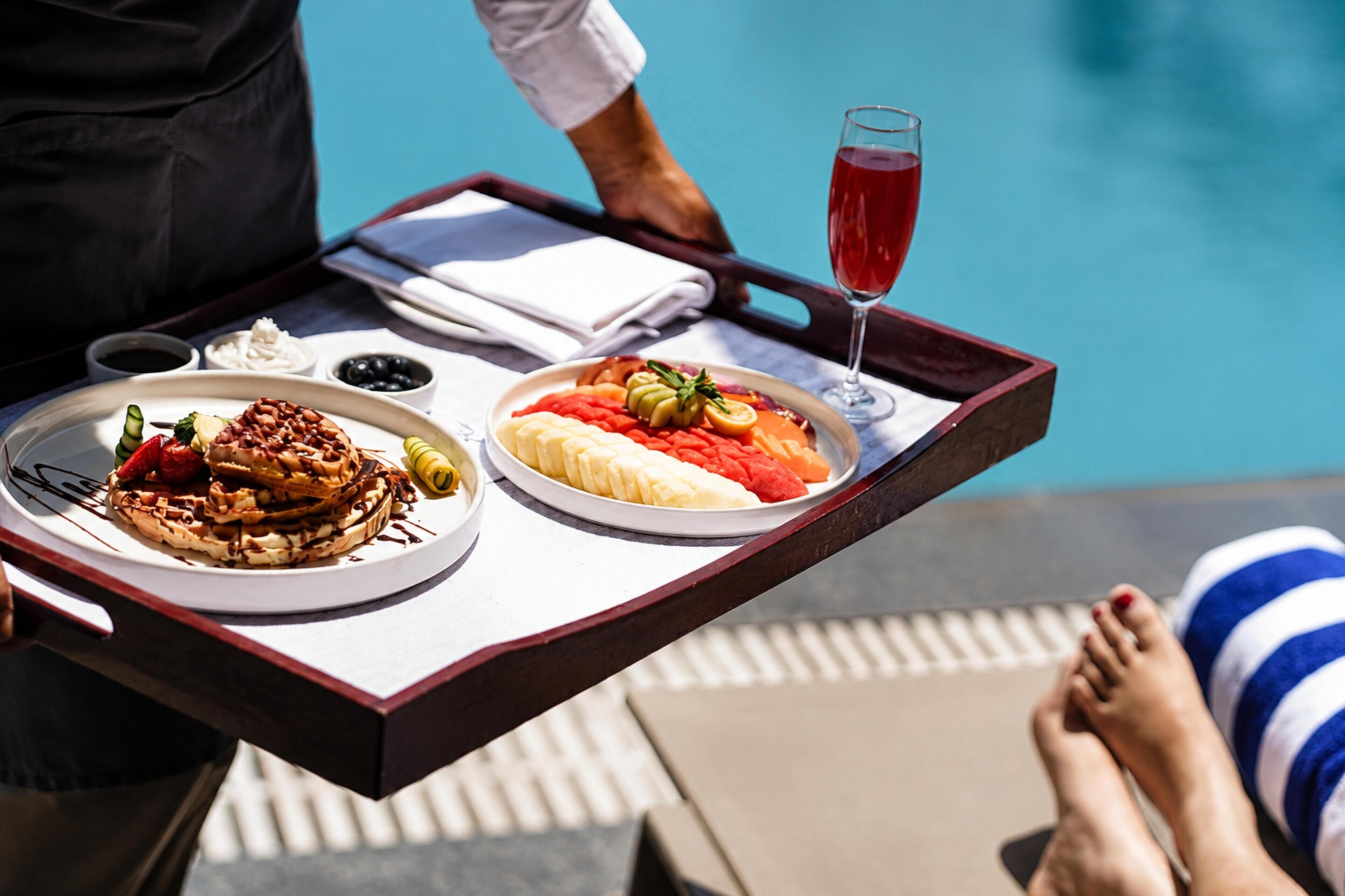 Bandeja con comida y una bebida, ambiente junto a la piscina, y una persona recostada.