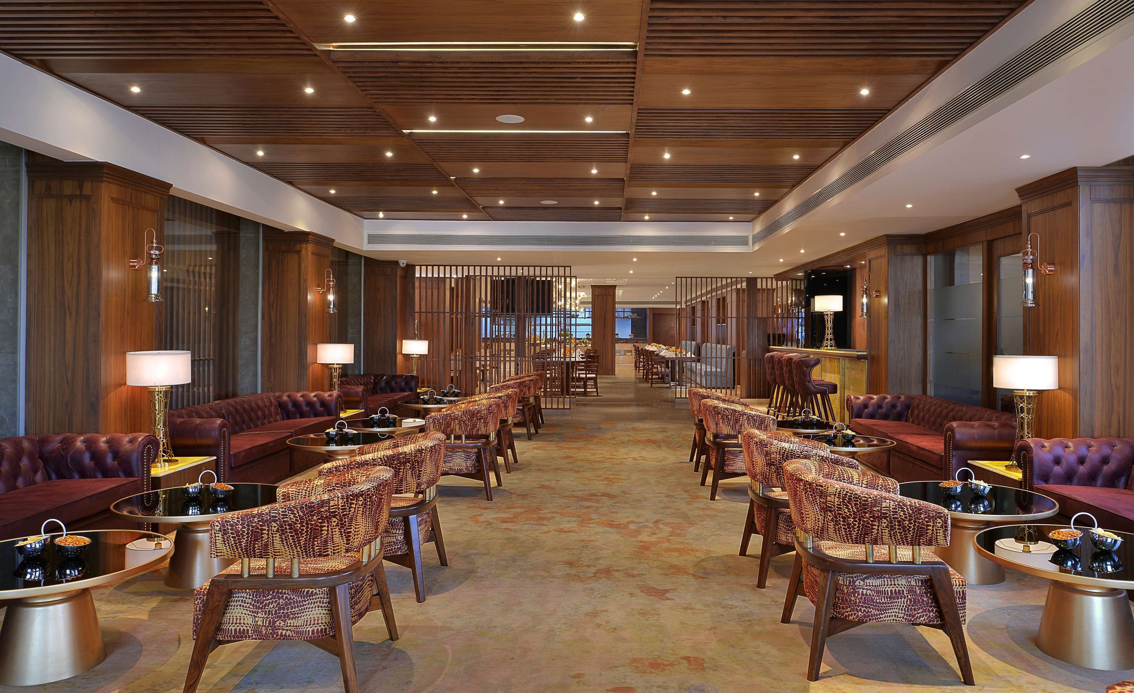 Un hall d’hôtel spacieux, doté de canapés en cuir, de fauteuils à motifs et d’un bar central.