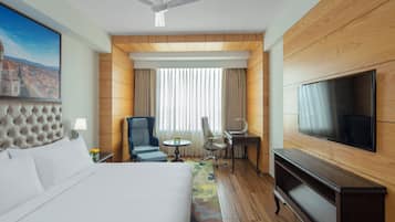 Une chambre d’hôtel équipée d’un lit, d’un bureau, d’une chaise, d’une télévision et d’un ventilateur de plafond.