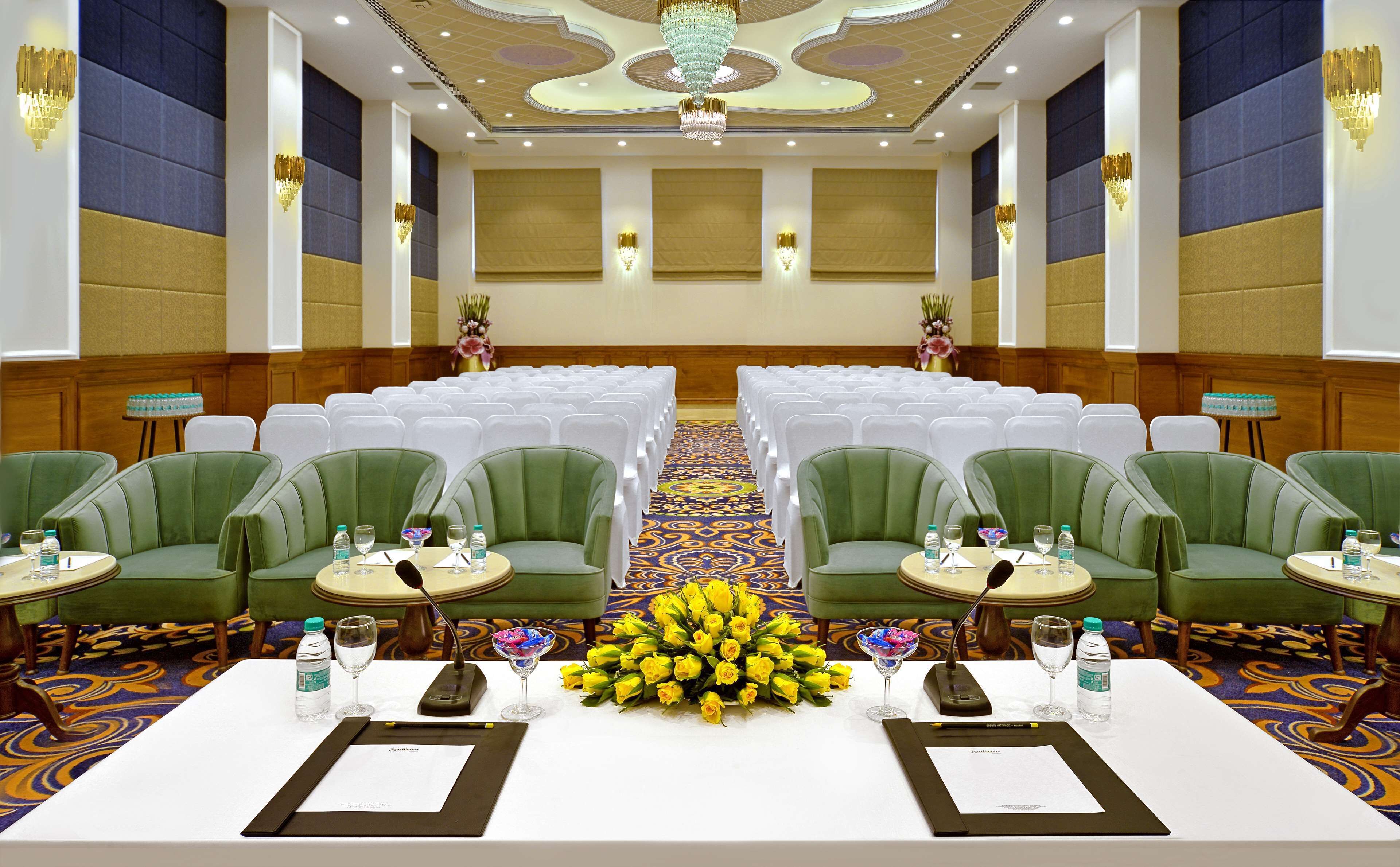 A conference room with rows of white chairs, green upholstered chairs, and a table with a floral centerpiece.