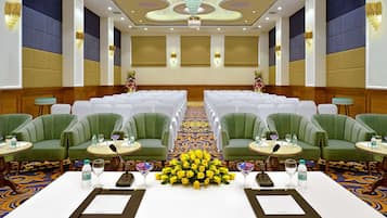 Un salón de conferencias con filas de sillas blancas, sillas tapizadas en verde y una mesa con un centro de mesa floral.