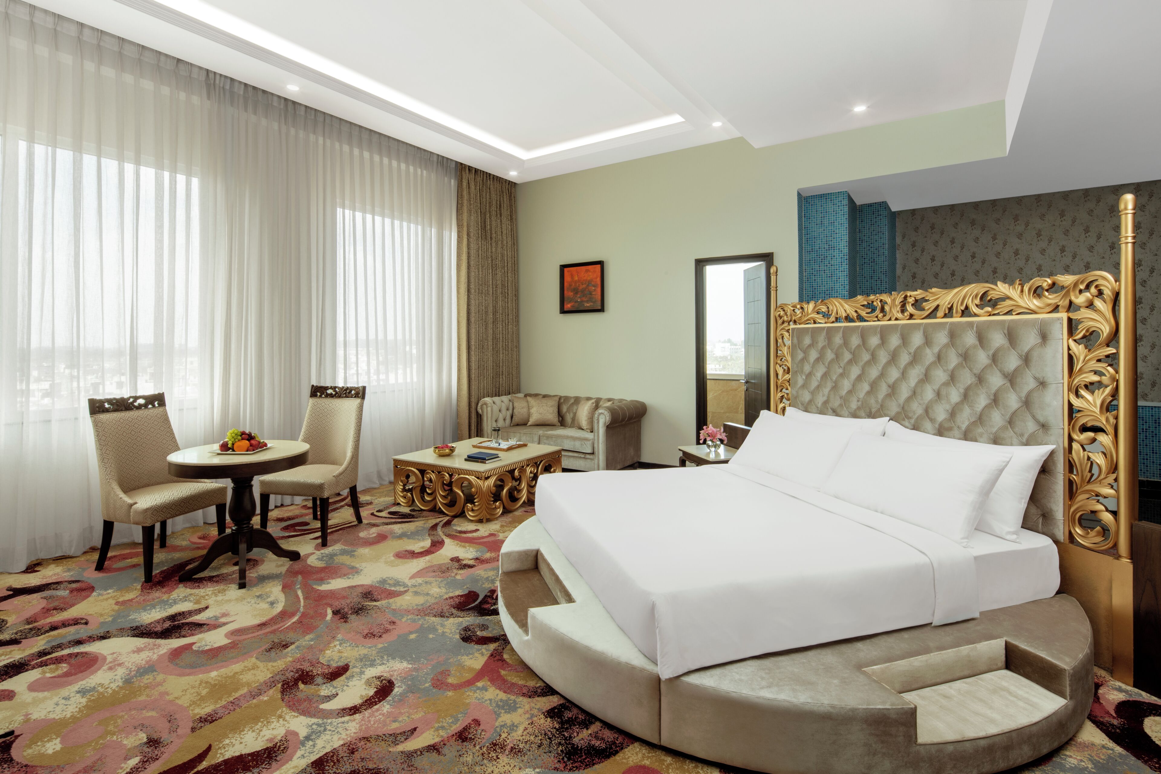 A hotel room with a large bed, a round seating area, a sofa, and a small table with a fruit bowl.