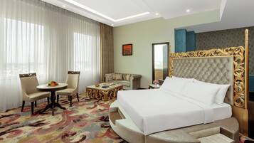 A hotel room with a large bed, a round seating area, a sofa, and a small table with a fruit bowl.