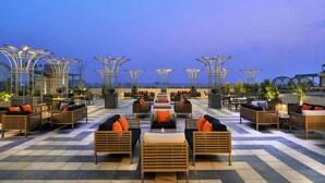 A rooftop lounge with outdoor seating and tables, featuring a checkered floor and a clear view of the city skyline at dusk. - Radisson Chandigarh Zirakpur (Dera Bassi)