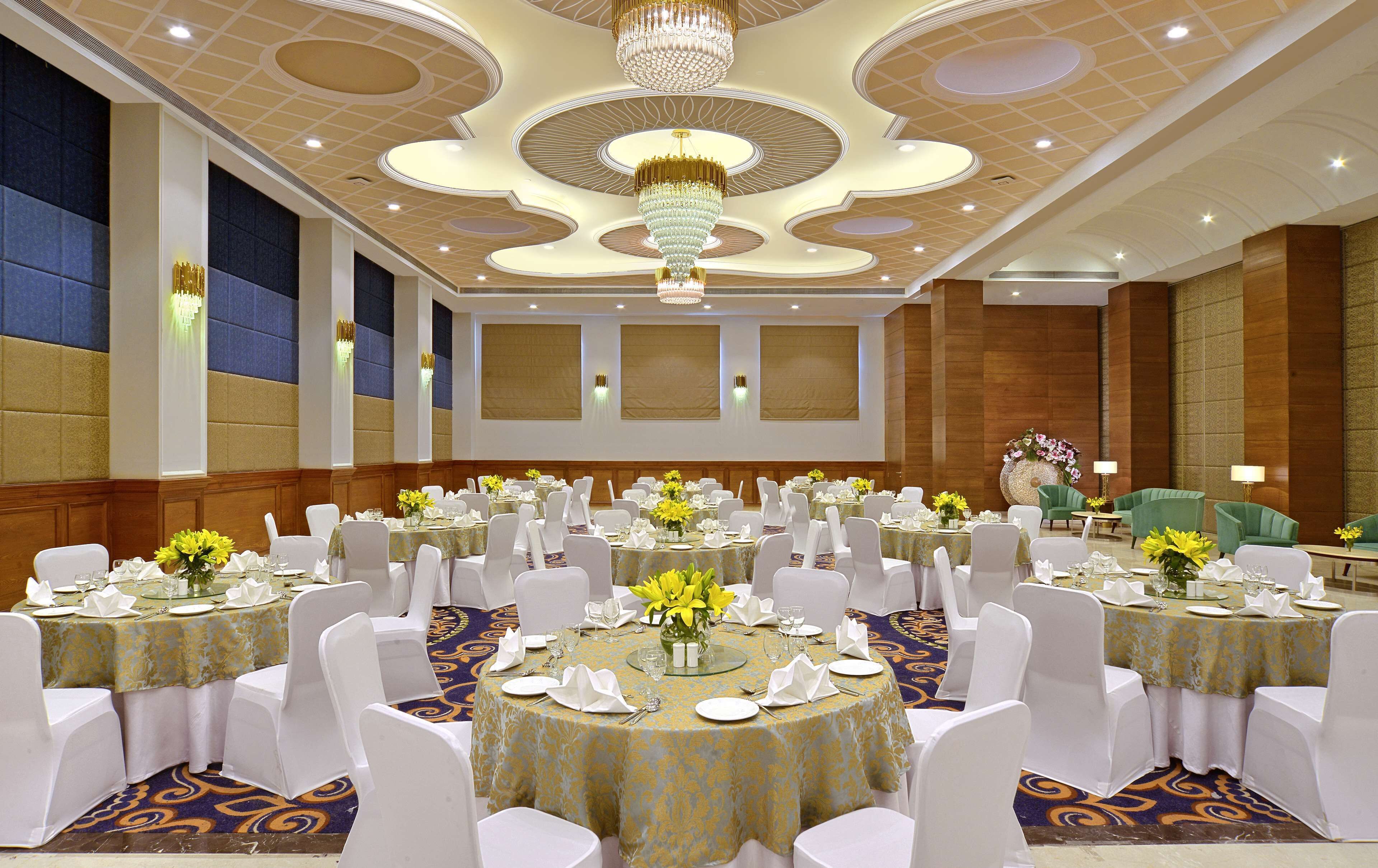 Un salón de banquetes con mesas redondas, sillas blancas y candelabros.