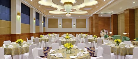 Un salón de banquetes con mesas redondas, sillas blancas y candelabros.