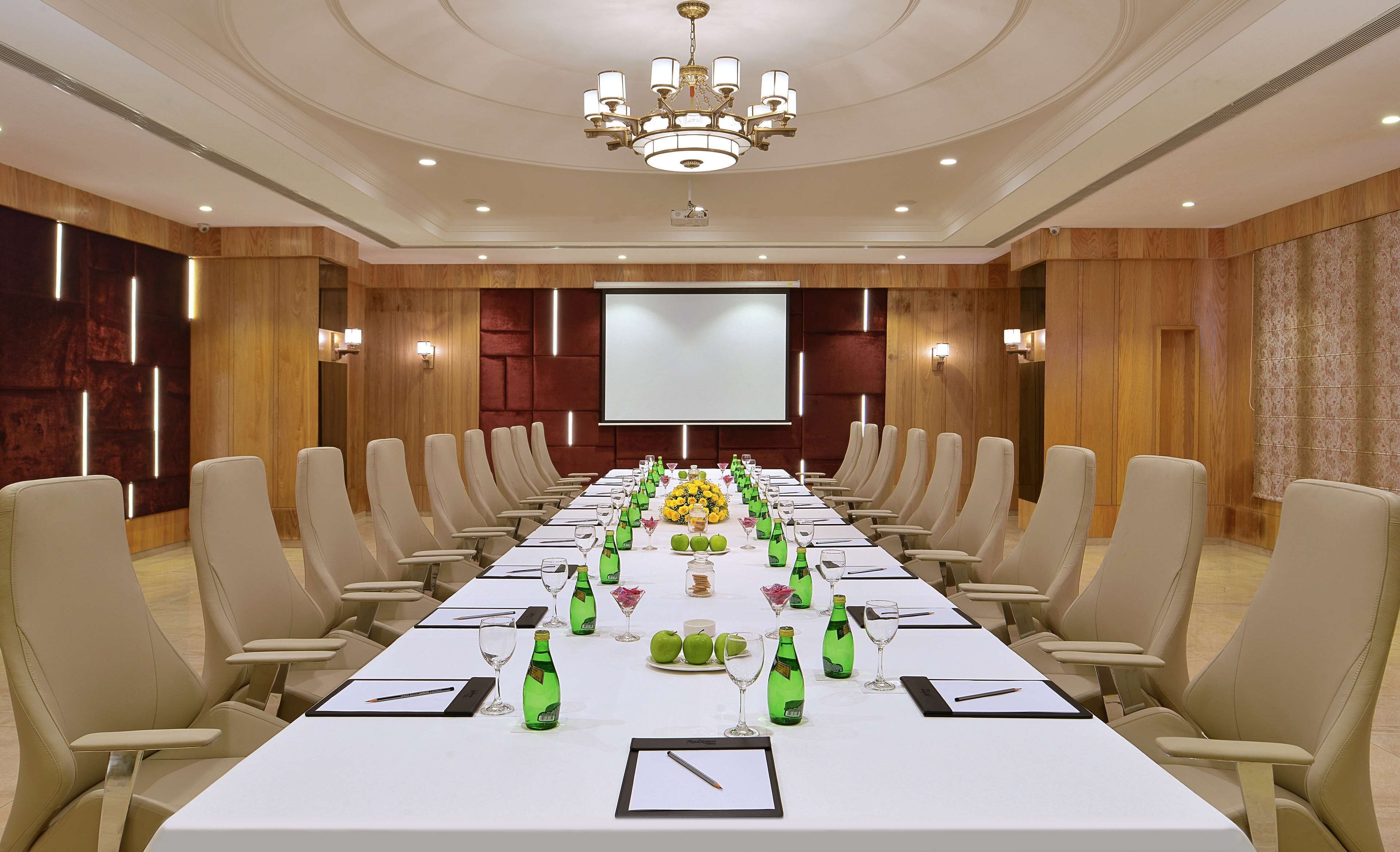 A conference room with a long table, chairs, a projector screen, and a chandelier.