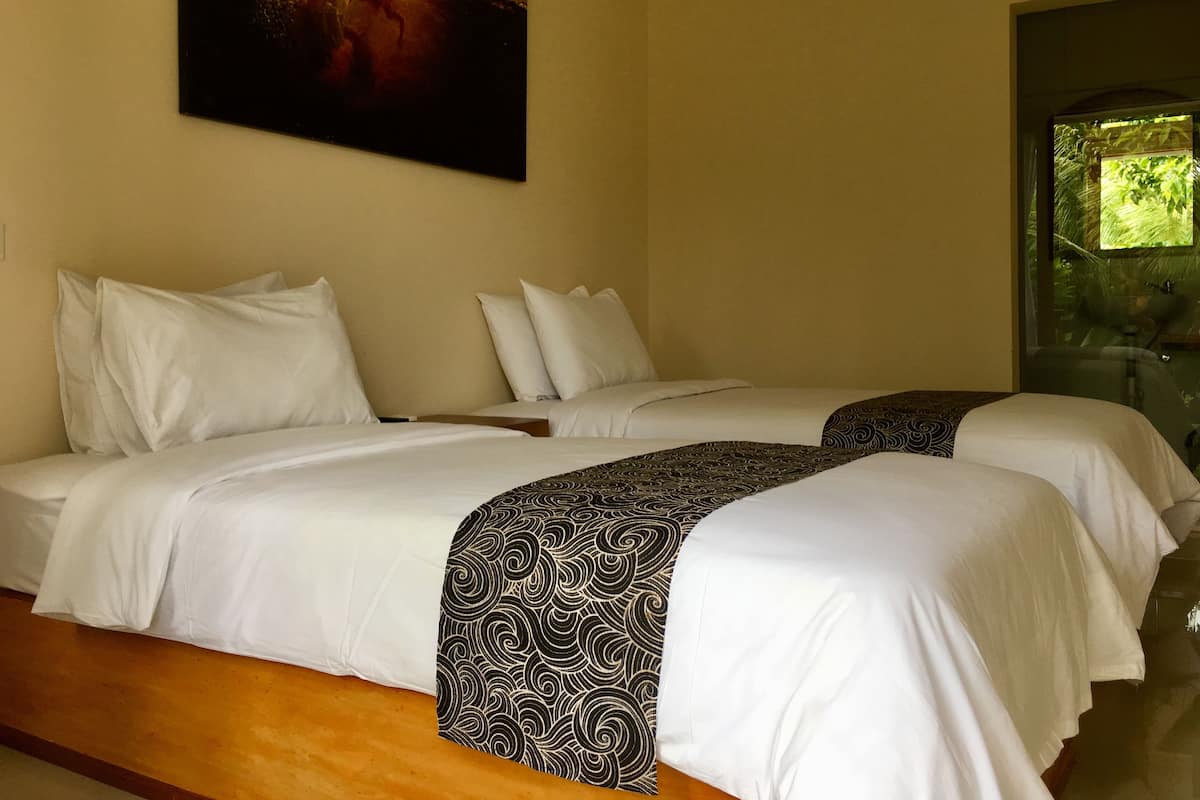 A hotel room with two beds, white bedding, a patterned throw, and a painting of a surfer on a wave.