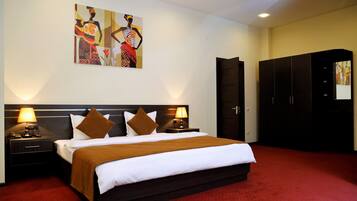 A hotel room with a large bed, two bedside tables with lamps, a wardrobe, and artwork on the walls.