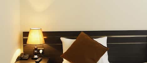 Habitación de hotel con cama, mesita de noche con lámpara y dos cuadros en la pared.