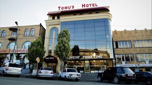 Hotel Tomu, con una fachada moderna, junto a un mercado y una tienda de alimentos.