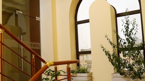 Un vestíbulo de hotel con una escalera de mármol, plantas en macetas y grandes ventanales.