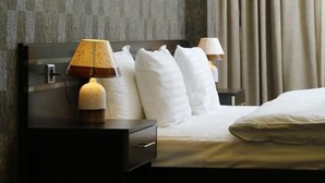 Una habitación de hotel con una cama, dos mesitas de noche, una lámpara y un aplique de pared.