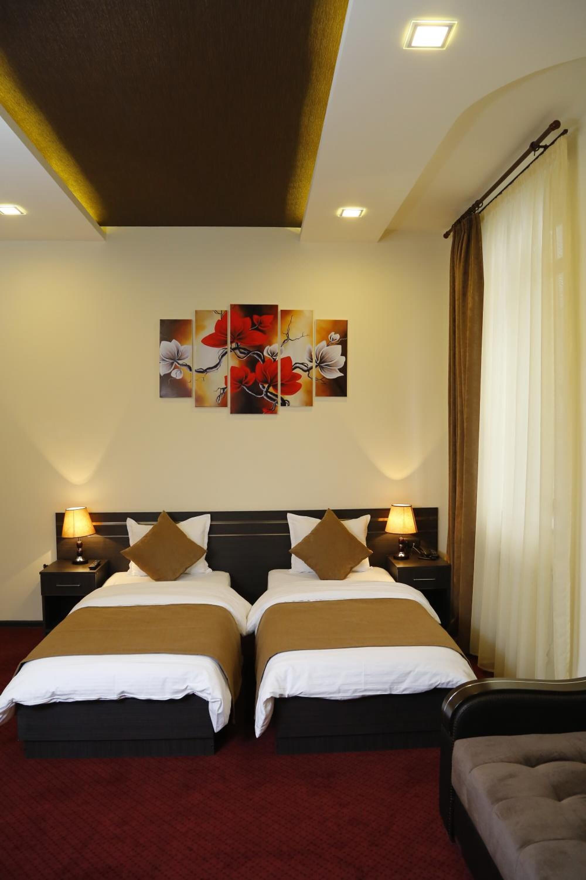 Habitación de hotel con dos camas, una alfombra roja, una obra de arte grande en la pared y una ventana con cortinas.