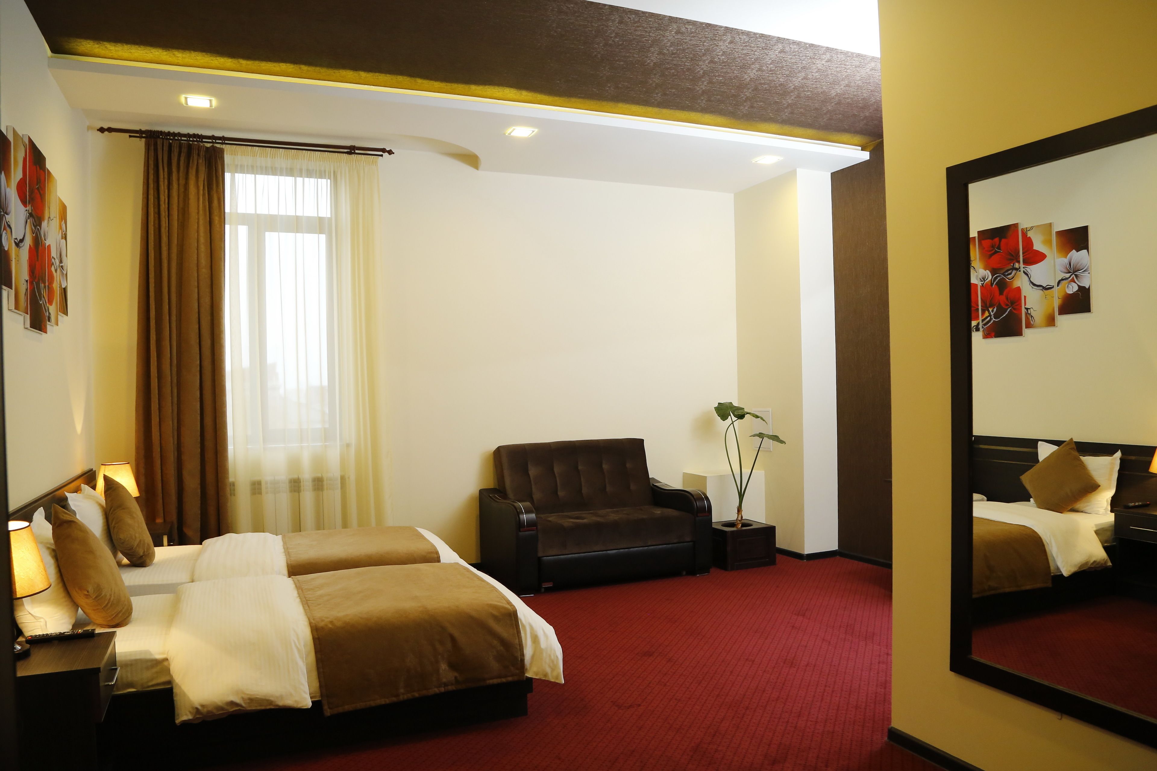 A hotel room with two beds, a sofa, a mirror, and a red carpet.